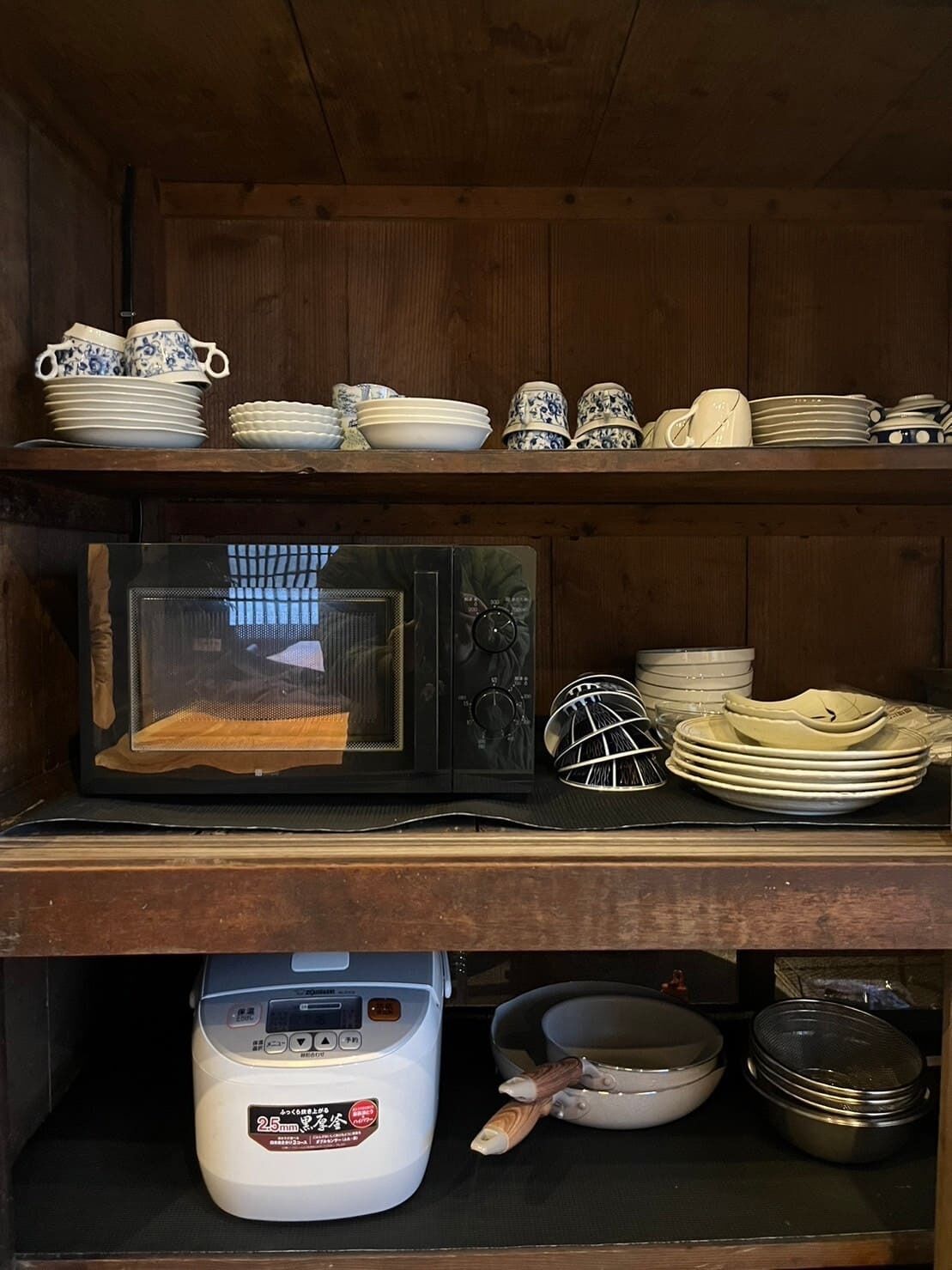 A kitchen with wooden shelves holding dishes and a microwave.
