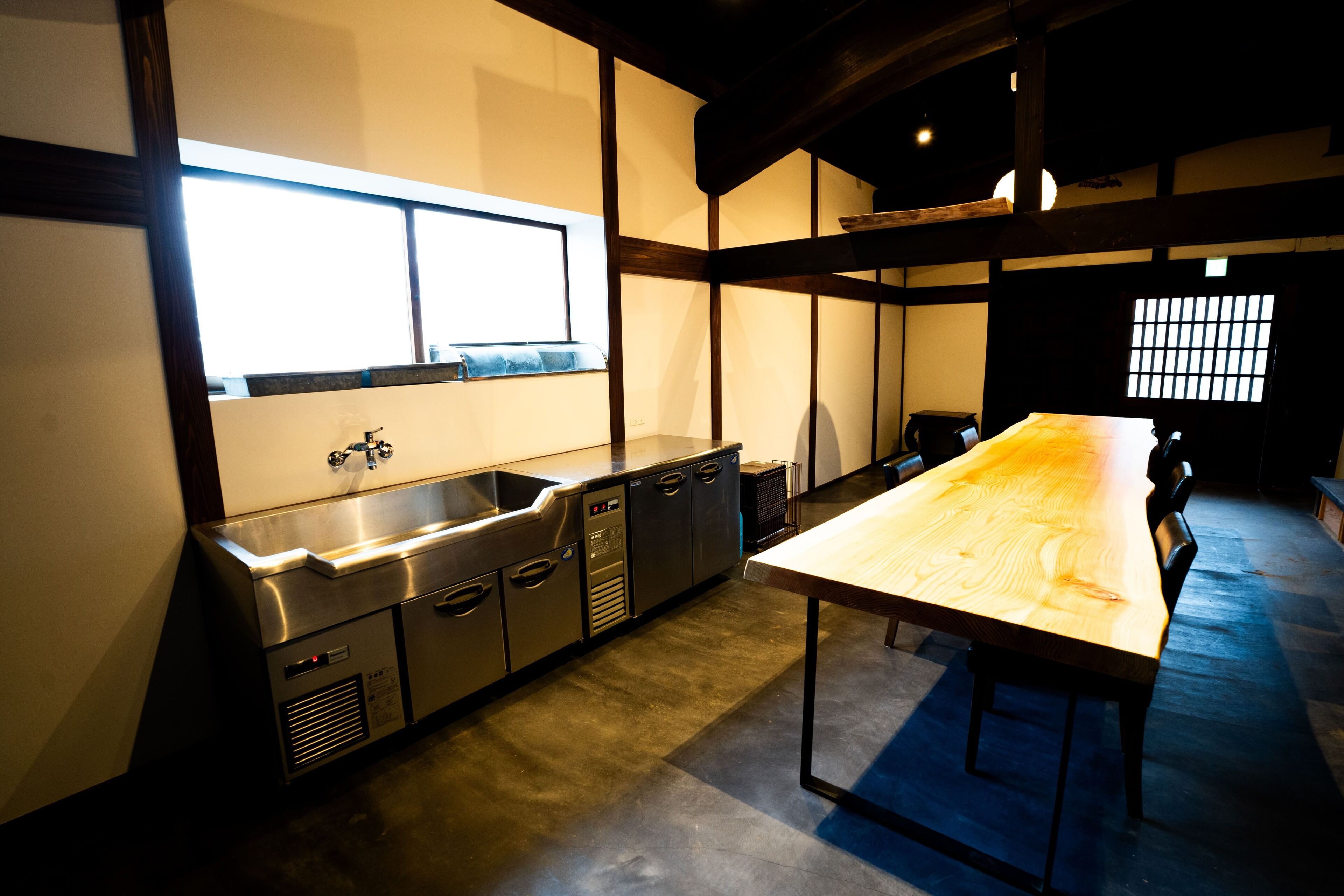 A modern kitchen with stainless steel appliances, a long wooden table, and a window providing natural light.