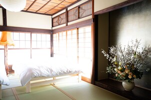 Una habitación japonesa tradicional con suelo de tatami, una cama baja de madera y un gran ventanal con puertas correderas.