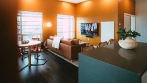 A modern living room with a sofa, dining table, and chairs, a TV mounted on the wall, and a large window. - *Free Parking* Cozy 2br/2ba Penthouse DT Halifax! (Halifax)
