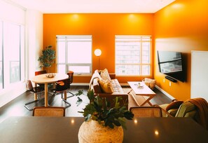Een moderne woonkamer met een bank, eettafel, stoelen, een plant en een televisie.