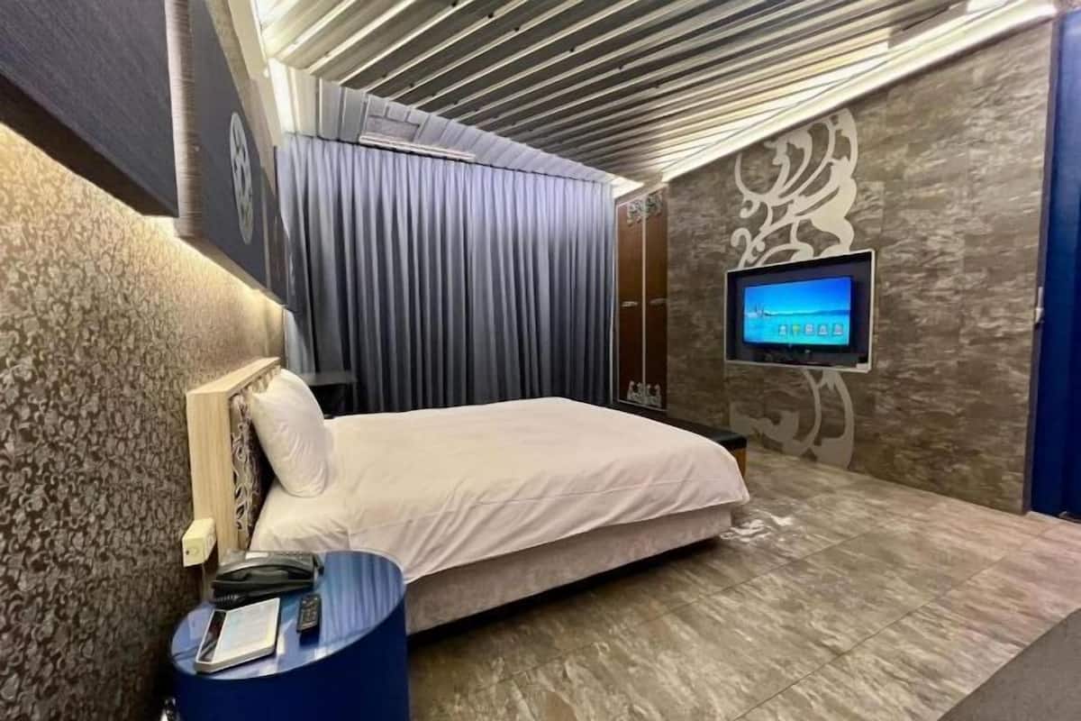 A hotel room with a bed, a TV mounted on the wall, a blue side table, and a patterned wall.