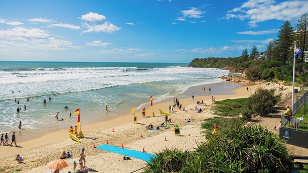 A beach with people, lifeguard flags, and a clear sky. - Dog Friendly Retreat with Pool & Stunning Hinterland Views (Ninderry)