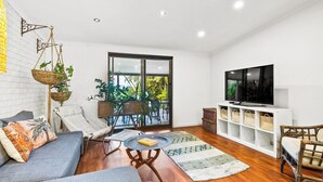 A modern living room with a sofa, a coffee table, a TV, and a balcony with plants. - Dog Friendly Retreat with Pool & Stunning Hinterland Views (Ninderry)