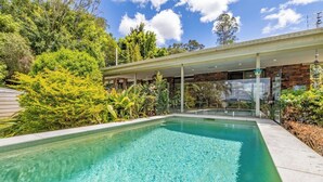 A rectangular pool with clear water, surrounded by lush greenery and a modern building with large windows. - Dog Friendly Retreat with Pool & Stunning Hinterland Views (Ninderry)