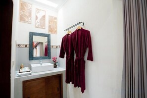 Un baño con espejo, lavabo y dos batas colgadas en un perchero.