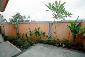 A courtyard with a low orange wall, potted plants, and a paved area. - Moning Villa Ubud (Bali)