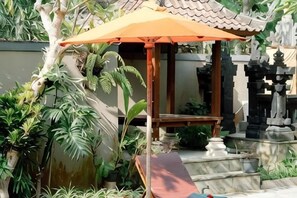 A traditional structure with an umbrella, surrounded by plants and stone elements. - Moning Villa Ubud (Bali)