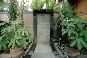 A gated entrance with a concrete door, surrounded by potted plants and a small pathway. - Moning Villa Ubud (Bali)