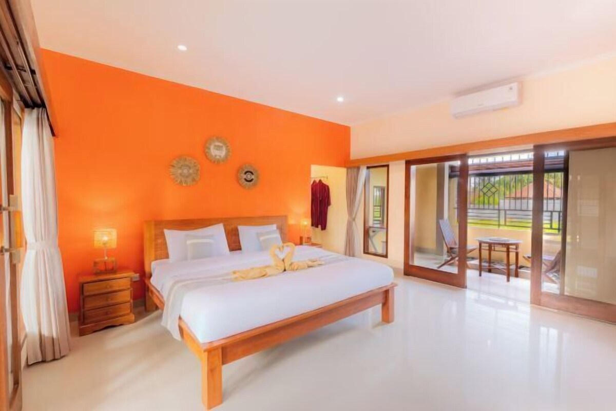 A bedroom with a large bed, a nightstand, a lamp, and a view through a glass door to an outdoor area.