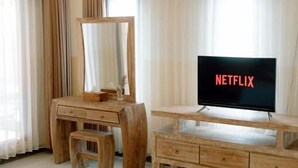 A wooden vanity with a mirror, a television displaying the Netflix logo, and a small stool. - Moning Villa Ubud (Bali)