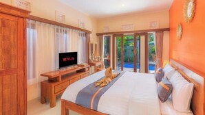 A hotel room with a bed, a TV, a desk, and a view of a swimming pool. - Moning Villa Ubud (Bali)