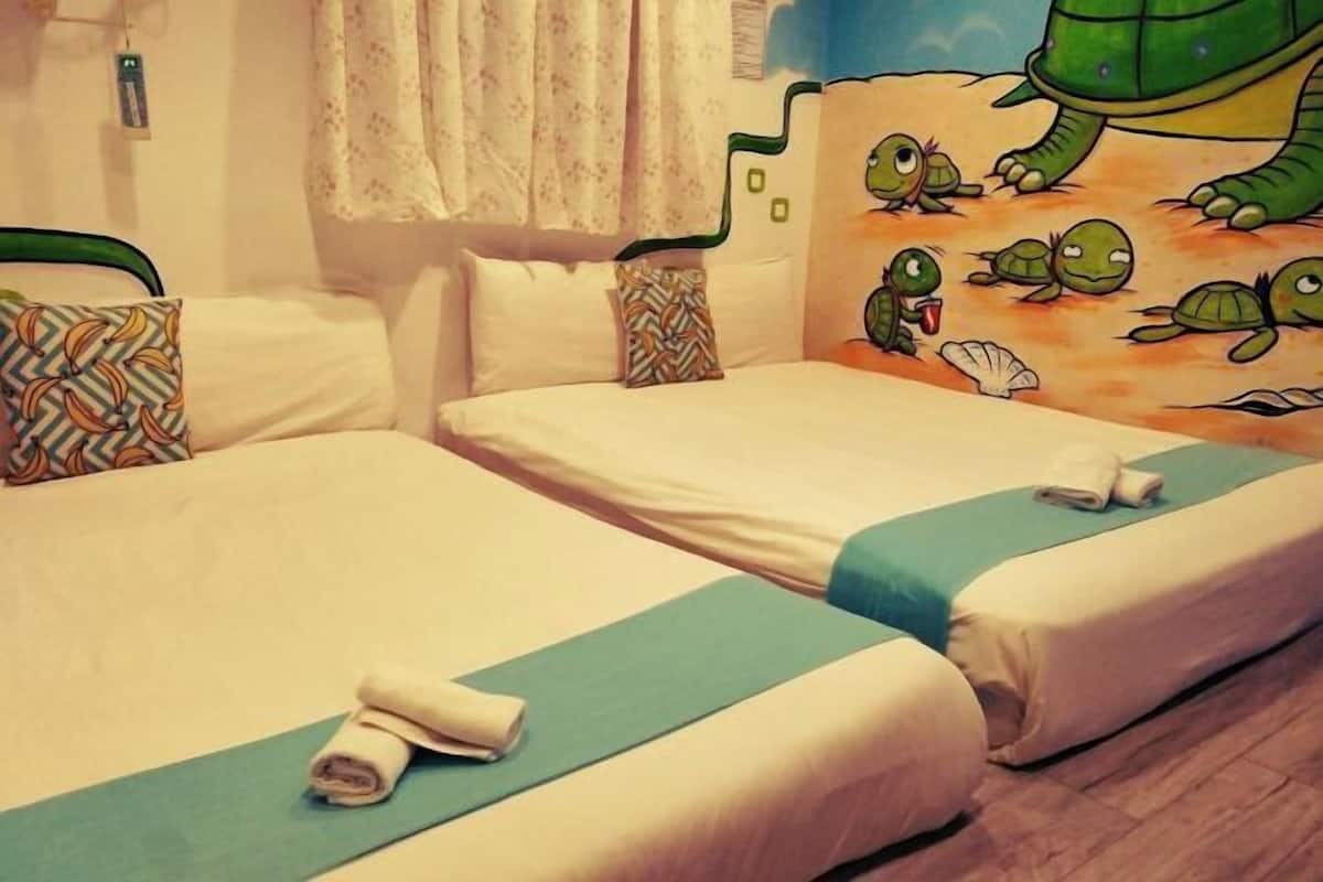 Habitació d'hotel amb dos llits, un mural de testudons i una finestra amb cortines.