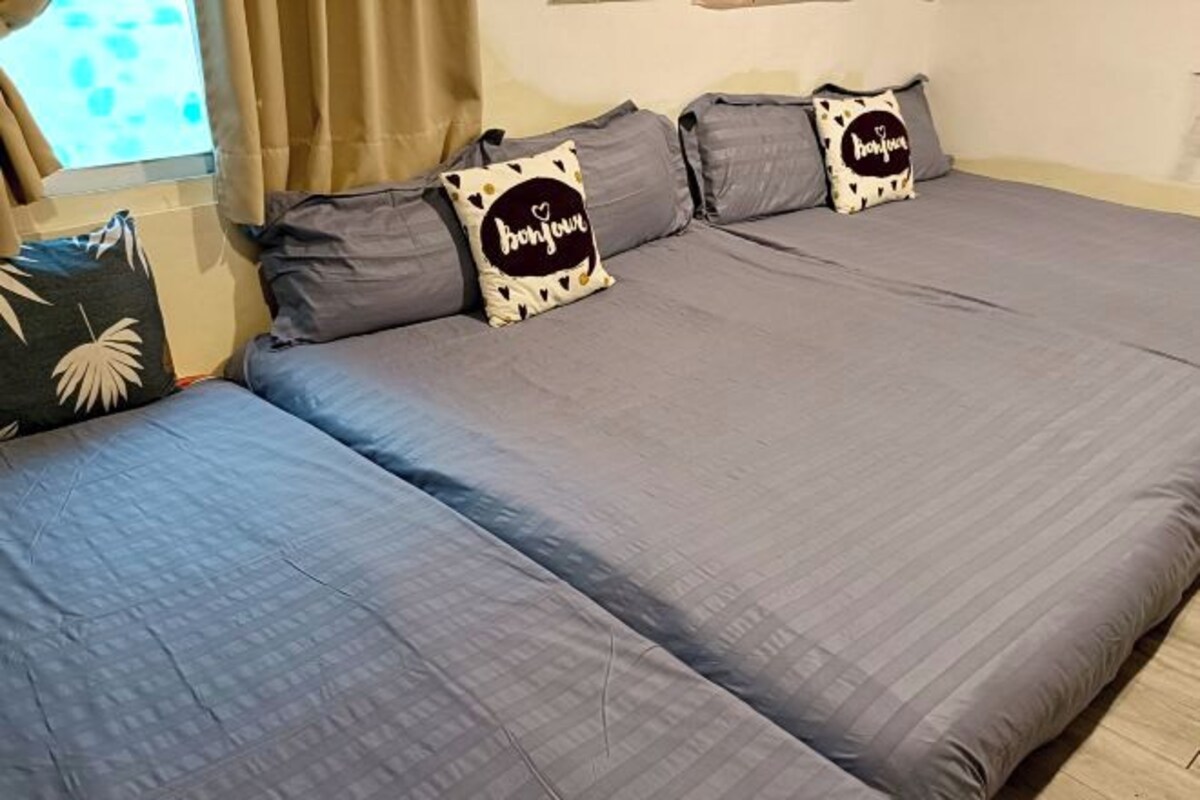 A double bed with grey bedding and two pillows with 'bonjour' text.