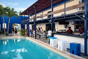 A poolside area with a bar and seating, surrounded by palm trees and a pool. - Hotel Chuburna (Progreso)