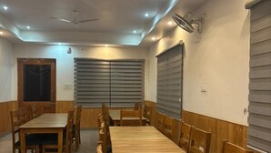 A dining area with wooden tables and chairs, recessed ceiling lights, and a ceiling fan. - Hotel Himalayan Park (Aut)