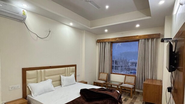 A hotel room with a bed, a desk, a chair, a TV, and a window with curtains. - Hotel Himalayan Park (Aut)