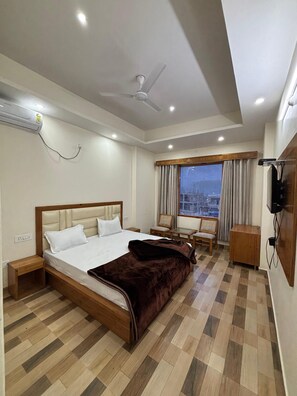 Une chambre d’hôtel avec un lit, un bureau, une chaise, une télévision et une fenêtre avec des rideaux.