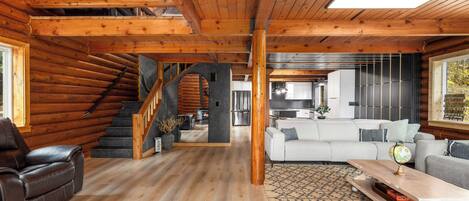 A spacious living area with a wooden staircase, a sofa set, and a dining table.