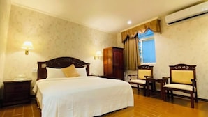 A hotel room with a large bed, two bedside tables, a wardrobe, a desk with chairs, and an air conditioning unit. - Fu Bao Motel (Hualien)