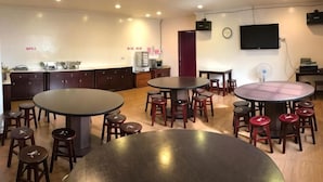 A spacious room with multiple round tables and stools, a kitchen area, and a flat-screen TV mounted on the wall. - Fu Bao Motel (Hualien)