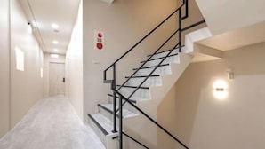 Een moderne trap met een geometrisch ontwerp, een lichtgekleurde gang en een zichtbare rookmelder.