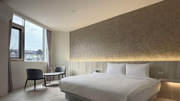 Een moderne hotelkamer met een groot bed, een kleintje tafel, twee stoelen en uitzicht op de stad.