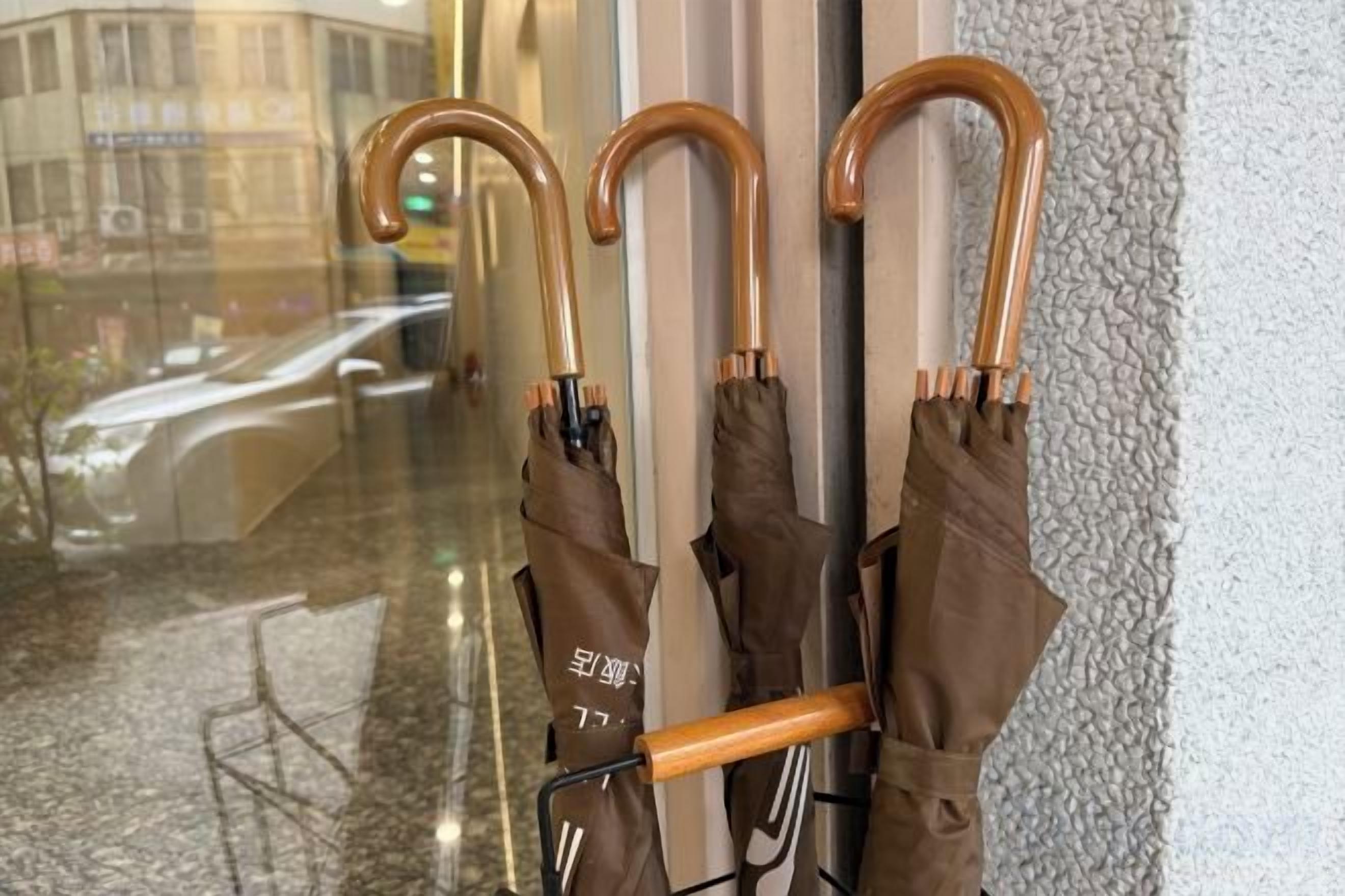 A row of umbrellas leaning against a wall with a reflection of a building and a car in the background.