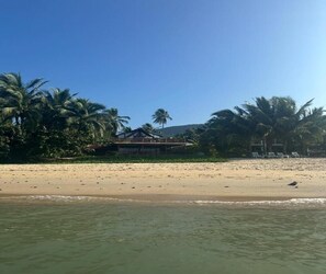 Ein Strand mit Palmen, sandigem Ufer und einem Gebäude mit schrägem Dach.