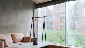 Een moderne woonkamer met een bank, een klein tafeltje en een groot raam met uitzicht op wolkenkrabbers.