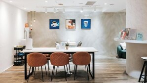 Een moderne vergaderruimte met een witte tafel, vier bruine stoelen en drie ingelijste foto’s aan de muur.