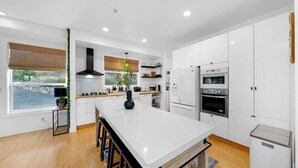 A modern kitchen with white cabinetry, a central island, and a view of the outdoors. - San Diego Serenity Hills, Pickleball, Golf, Infinity Pool with Epic Views (Jamul)