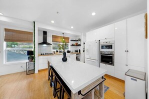 Une cuisine moderne avec des meubles blancs, un îlot central et une vue sur l’extérieur.