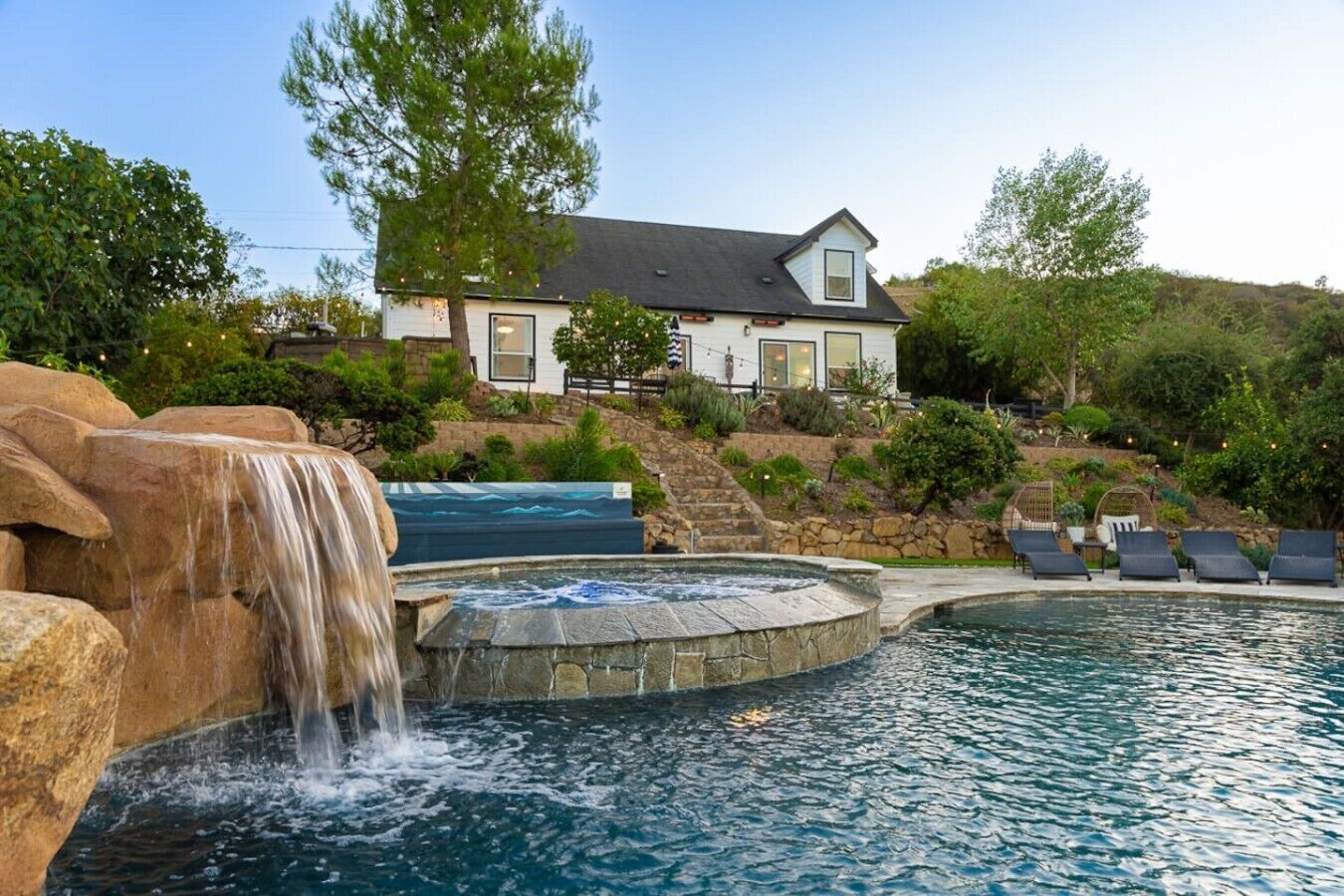 Ein Pool mit Wasserfall, ein Whirlpool und ein Haus im Hintergrund.