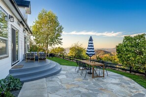 A patio with a table and chairs, a striped umbrella, and a view of the landscape.