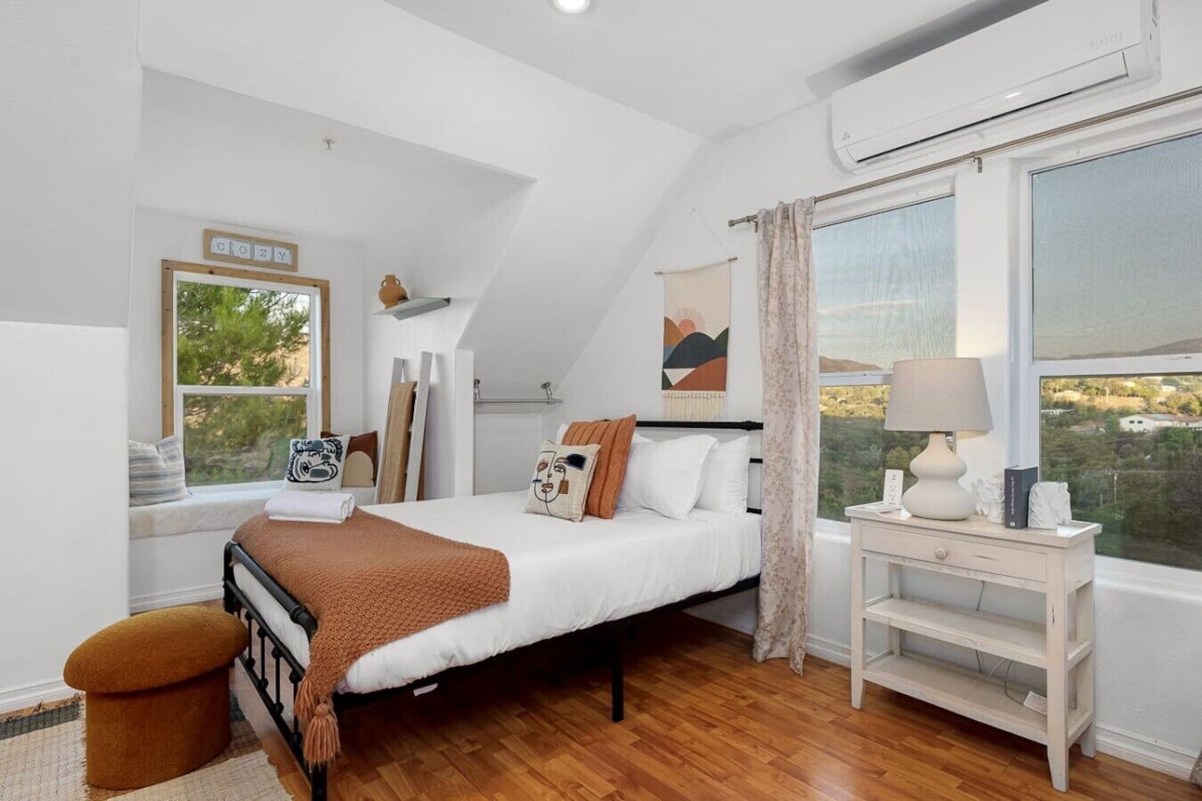 Un dormitorio con cama, mesita de noche con lámpara, ventana con vistas y aire acondicionado de pared.