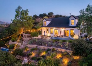 A two-story house with a well-maintained garden, a patio with outdoor furniture, and a visible staircase leading to the entrance.