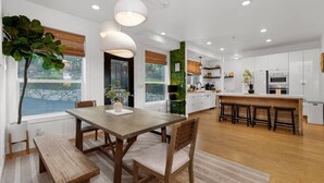 A modern kitchen with white cabinets, a wooden dining table, and pendant lights. - San Diego Serenity Hills, Pickleball, Golf, Infinity Pool with Epic Views (Jamul)