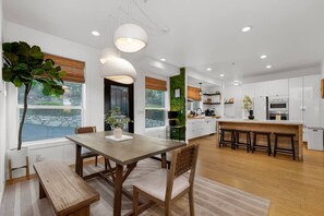 A modern kitchen with white cabinets, a wooden dining table, and pendant lights.