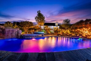 A swimming pool with a waterfall feature, surrounded by a landscaped garden and a house.
