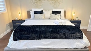 Una cama bien hecha con edredón blanco y negro, dos mesitas de noche con lámparas y decoración de pared.