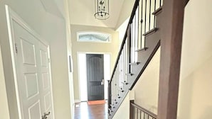 Un pasillo con piso de madera, una puerta blanca y una escalera con barandilla oscura.