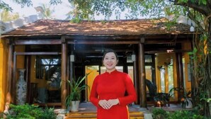A woman in a red dress standing in front of a traditional wooden structure with a tiled roof, surrounded by greenery. - Hoi An Phu Quoc Resort & Spa (Phu Quoc Island)
