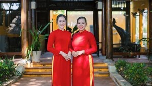 Two individuals in red dresses standing in front of a building with a sign that reads "HÀNH PHƯƠNG". - Hoi An Phu Quoc Resort & Spa (Phu Quoc Island)