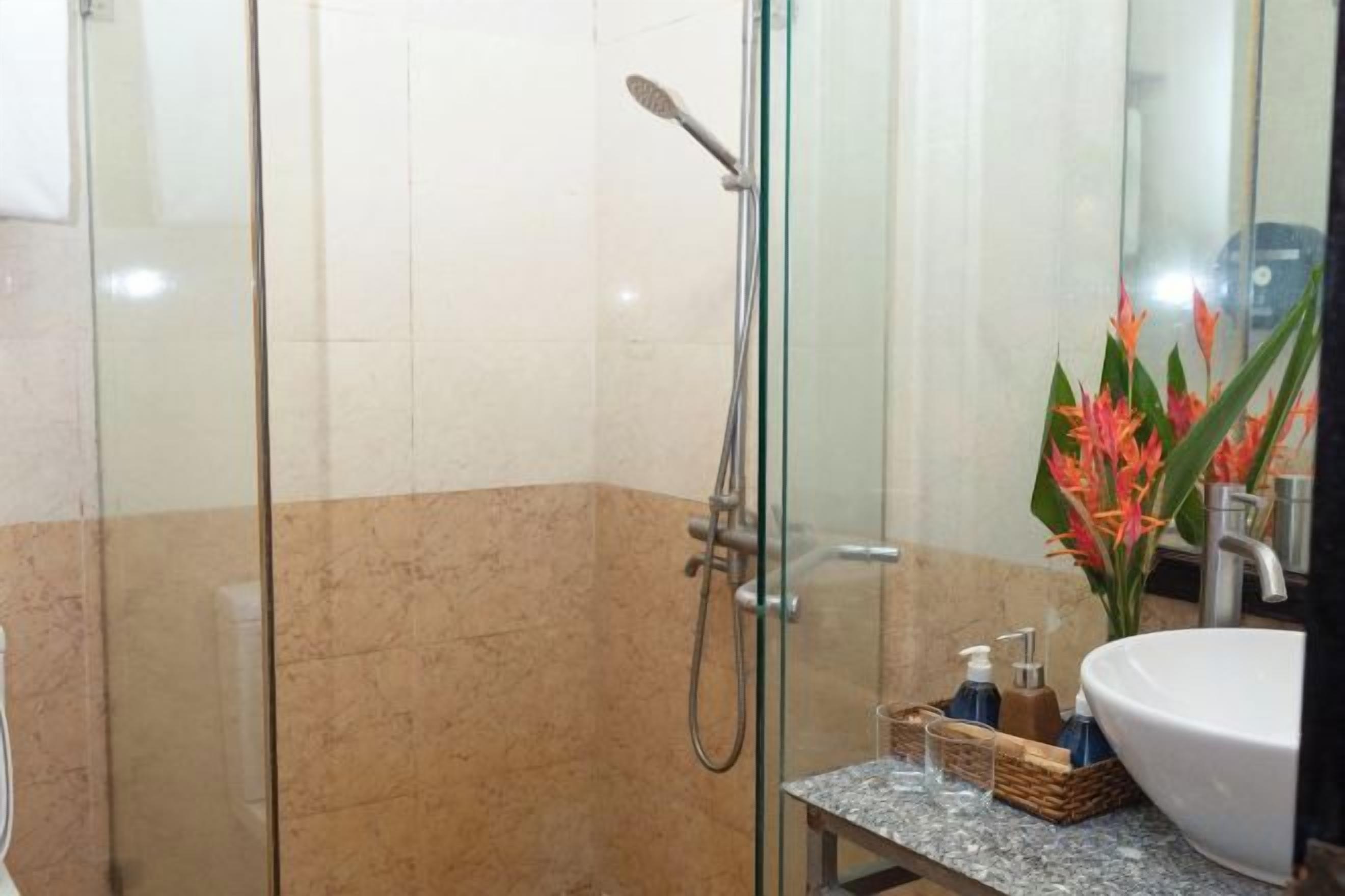 A glass-enclosed shower area with a handheld showerhead, a sink with a marble countertop, and a vase with flowers.