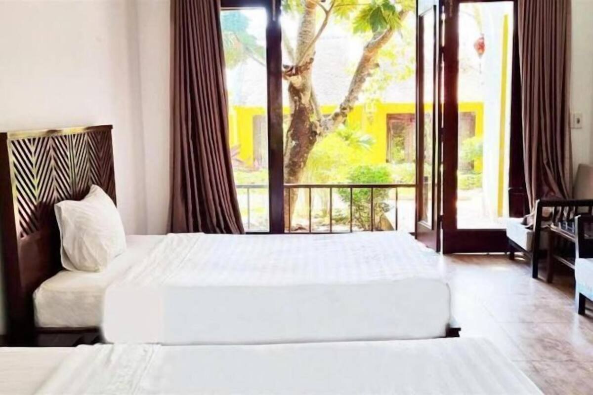 A hotel room with a bed, curtains, a view of the outdoors, and a balcony.