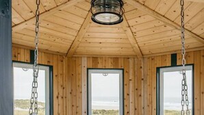 A wooden room with large windows, a hanging chair, and a small wooden table. - Lighthouse on the Beach with Hot Tub & Fire Pit (Manzanita)