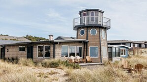 A coastal house with a prominent tower structure, large windows, and outdoor seating area. - Lighthouse on the Beach with Hot Tub & Fire Pit (Manzanita)