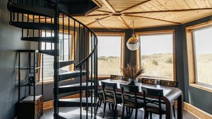 A room with a spiral staircase, a dining table with chairs, and large windows offering a view of the outdoors. - Lighthouse on the Beach with Hot Tub & Fire Pit (Manzanita)