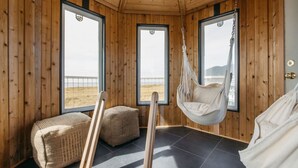 A wooden cabin room with large windows, a hanging chair, and two woven poufs. - Lighthouse on the Beach with Hot Tub & Fire Pit (Manzanita)